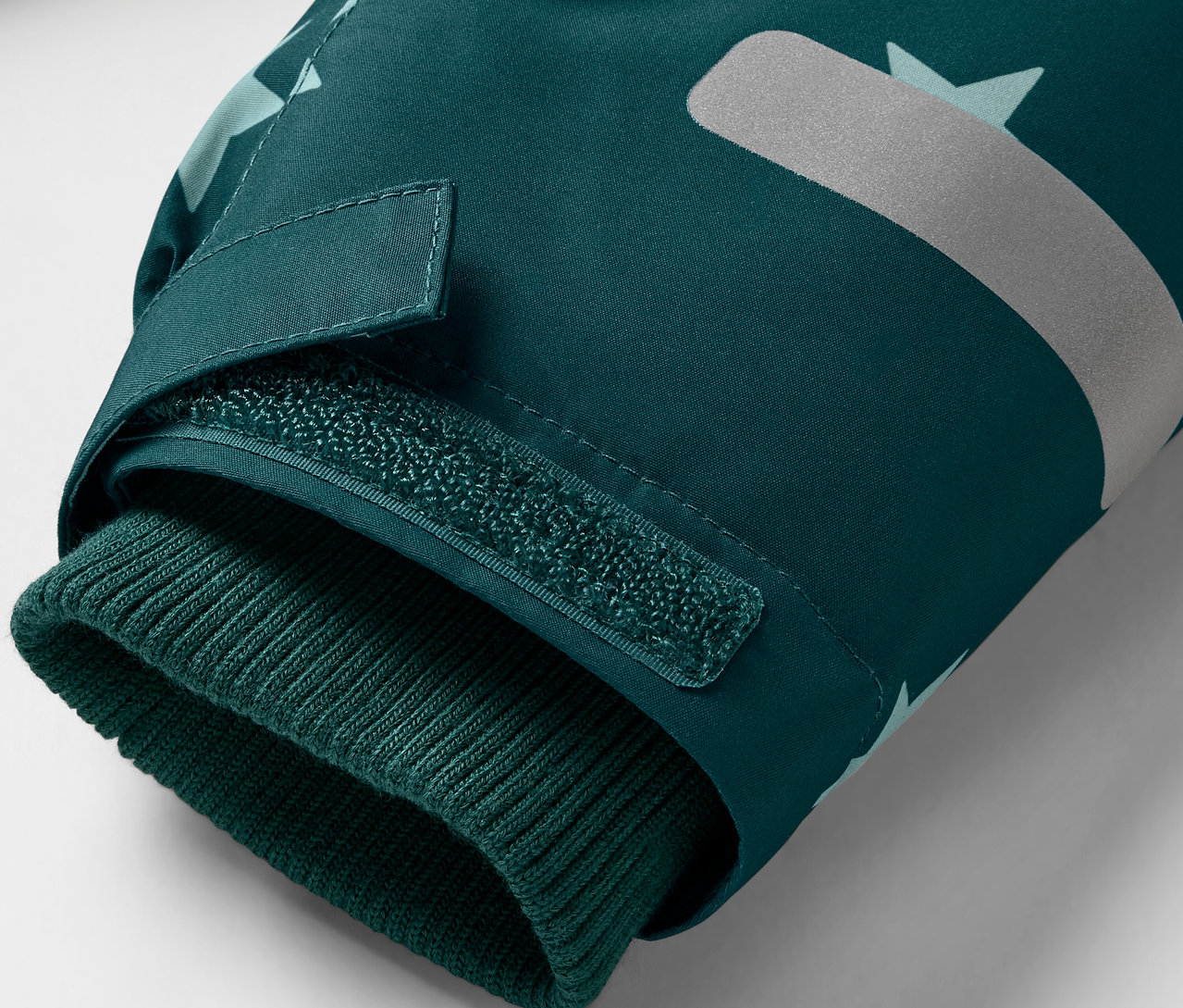 Detail tmavozelenej bundy s pleteným lemom na rukáve a reflexným prvkom.