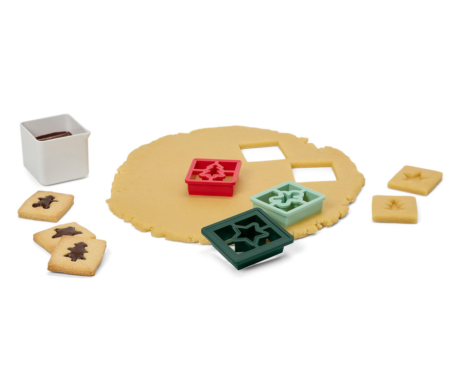 Cesto s vykrajovátkami v tvare stromčeka, hviezdy a ozdoby, hotové sušienky a biela nádoba s polevou.