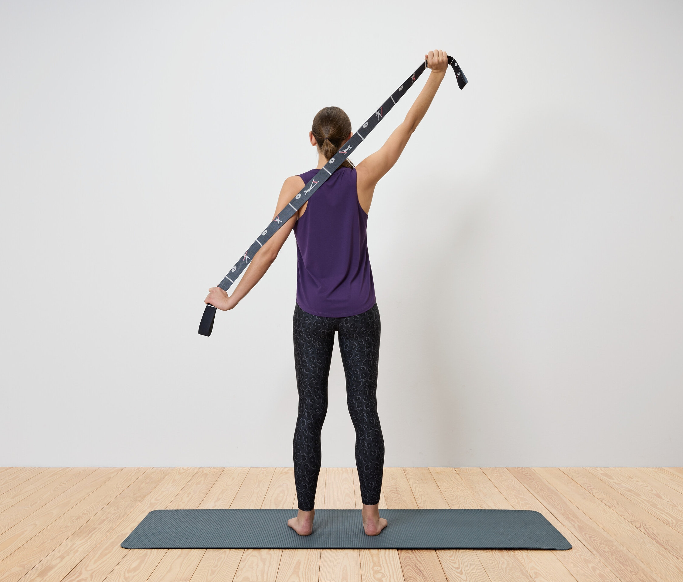 Žena si naťahuje hornú časť tela pomocou popruhu na jogu.