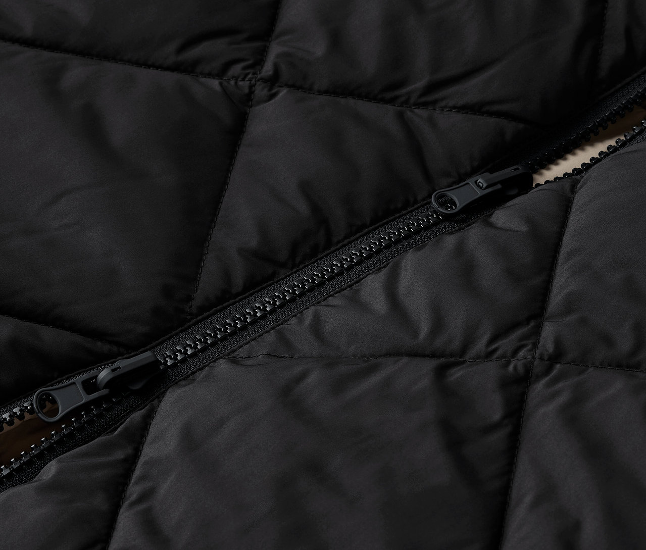 Detail čiernej prešívanej bundy so zipsom.