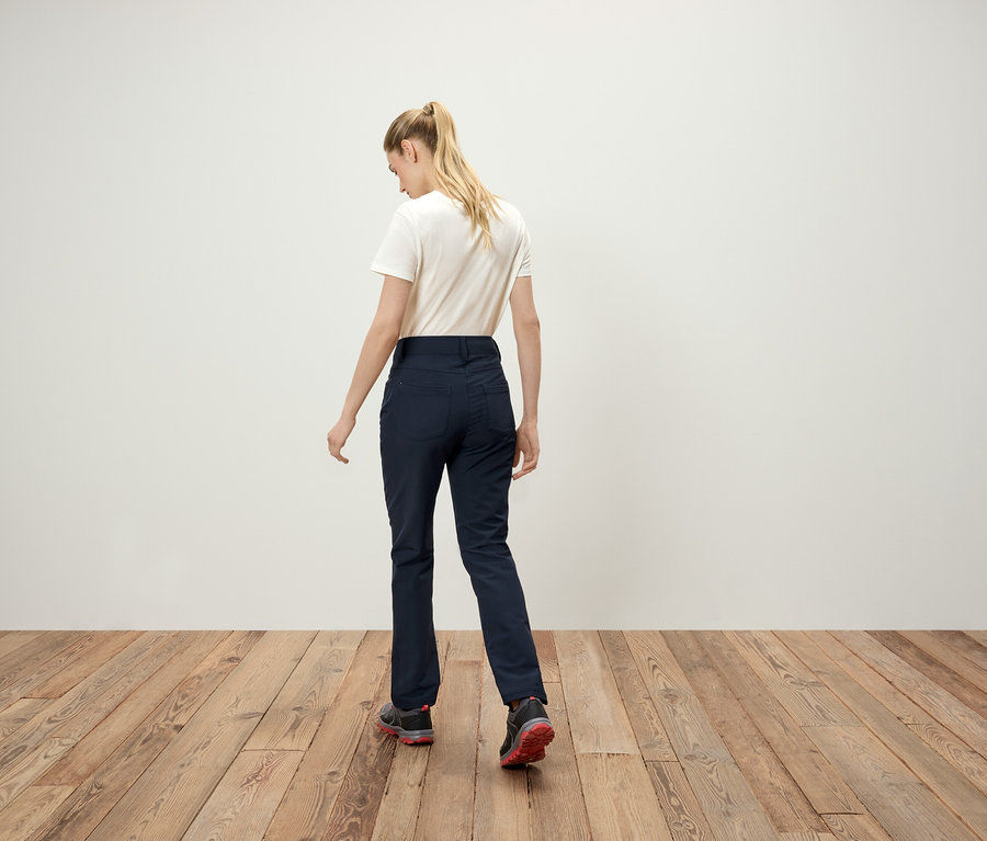 Zozadu je vidieť ženu s blond vlasmi v cope, bielom tričku, tmavomodrých nohaviciach a športových topánkach.