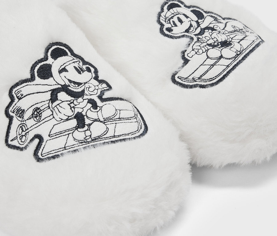 Detail bielych chlpatých papúč s kreslenými obrázkami Mickey Mouse na saniach.