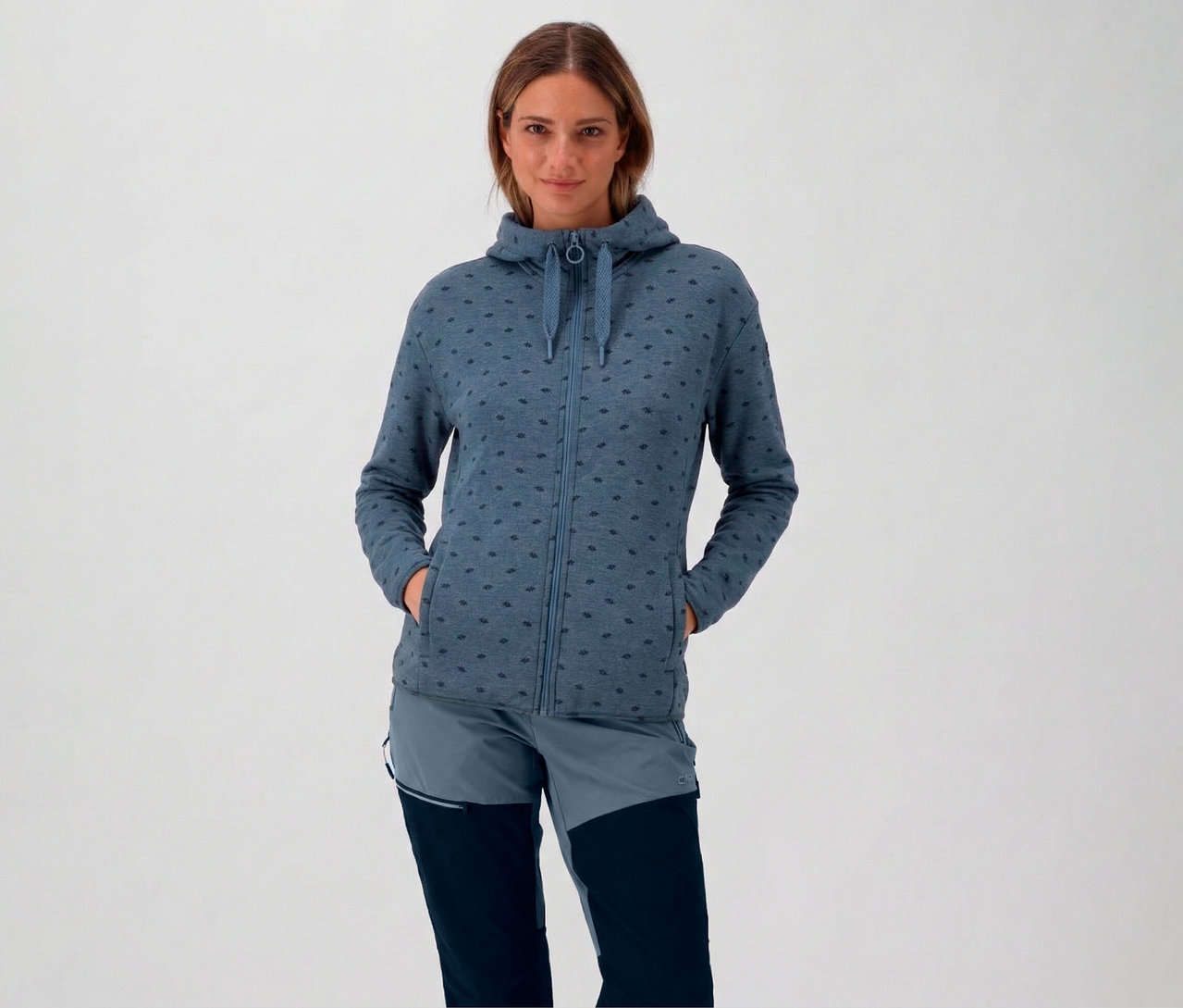 Žena v modrej flísovej bunde CMP s kapucňou a rukami vo vreckách.