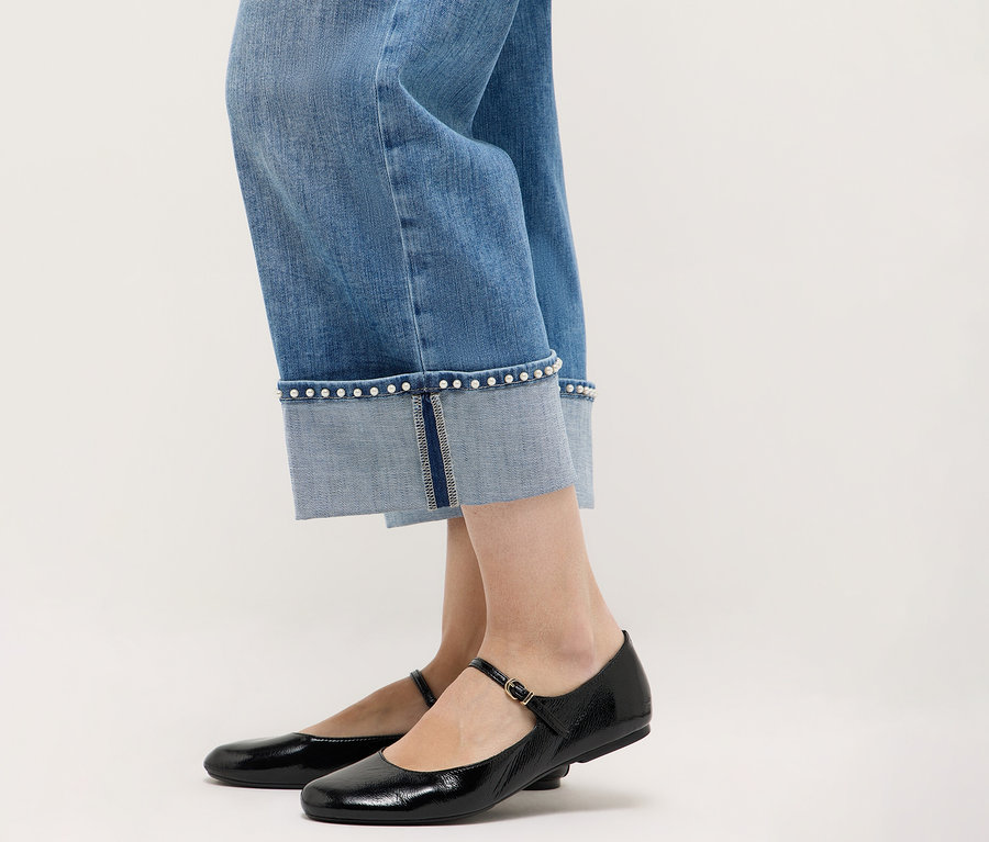 Detailný záber na nohy v džínsoch Angels Denim »Linn Cool« v kombinácii s čiernymi topánkami Mary Jane na neutrálnom pozadí.
