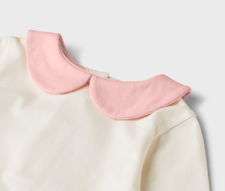Detailný pohľad na krémový top s ružovým okrúhlym golierom.