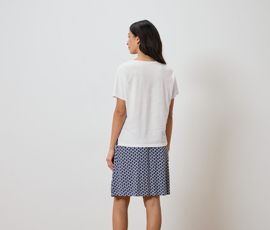 Pohľad zozadu na ženu s tmavými vlasmi v bielom tričku a sukni s modrým vzorom.