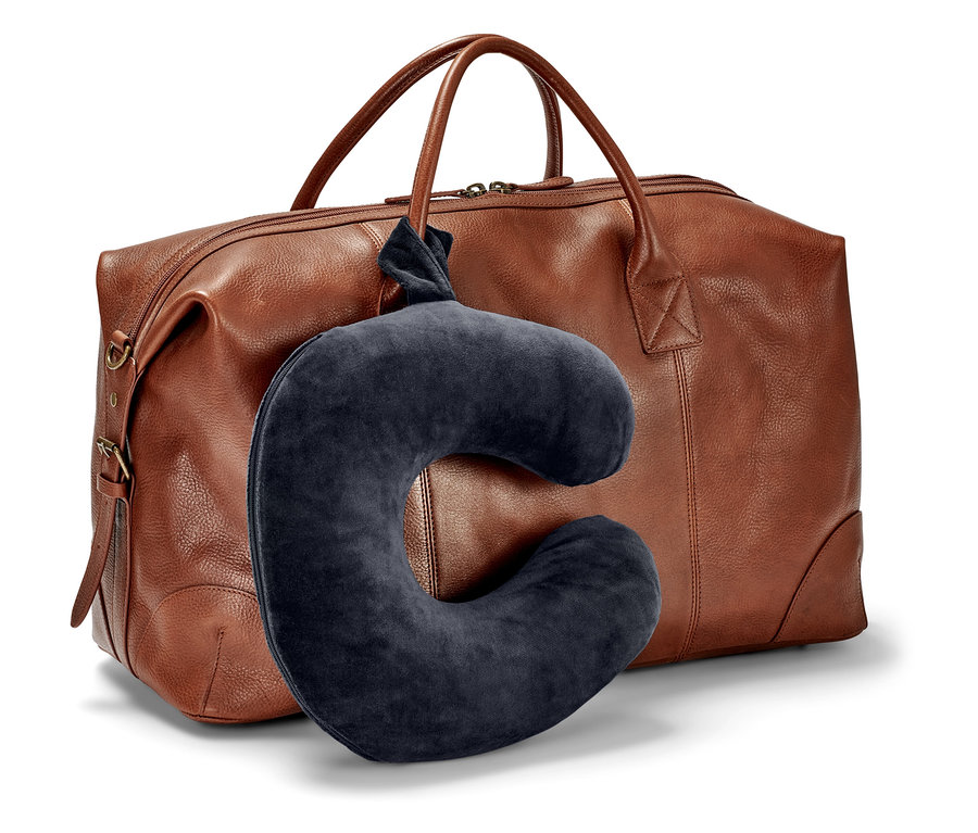 Tmavomodrý cestovný vankúš visí pred hnedou cestovnou taškou.