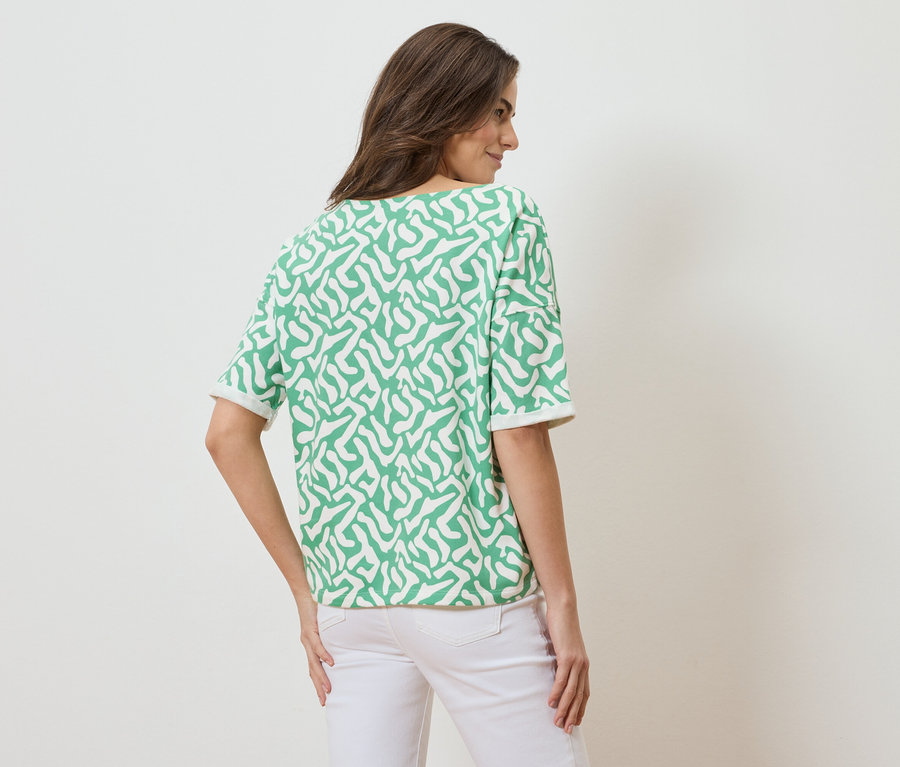 Pohľad zozadu na ženu s hnedými vlasmi v zeleno-bielom vzorovanom tope s krátkym rukávom a bielych džínsoch.