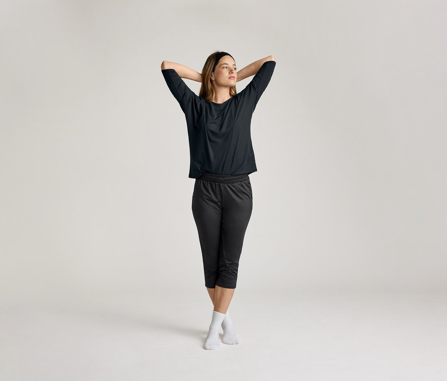 Žena so spojenými rukami za hlavou má na sebe čierne 3/4 športové tričko.