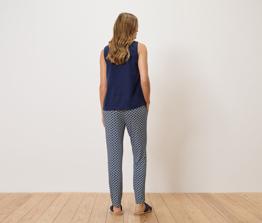 Žena stojí chrbtom k fotoaparátu a má na sebe tmavomodrý top a vzorované nohavice.