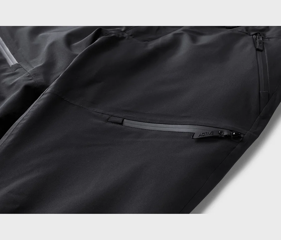 Detail čiernych nohavíc s vreckami na zips a reflexným pásikom. Na jazdci zipsu je nápis "ACTIVE".