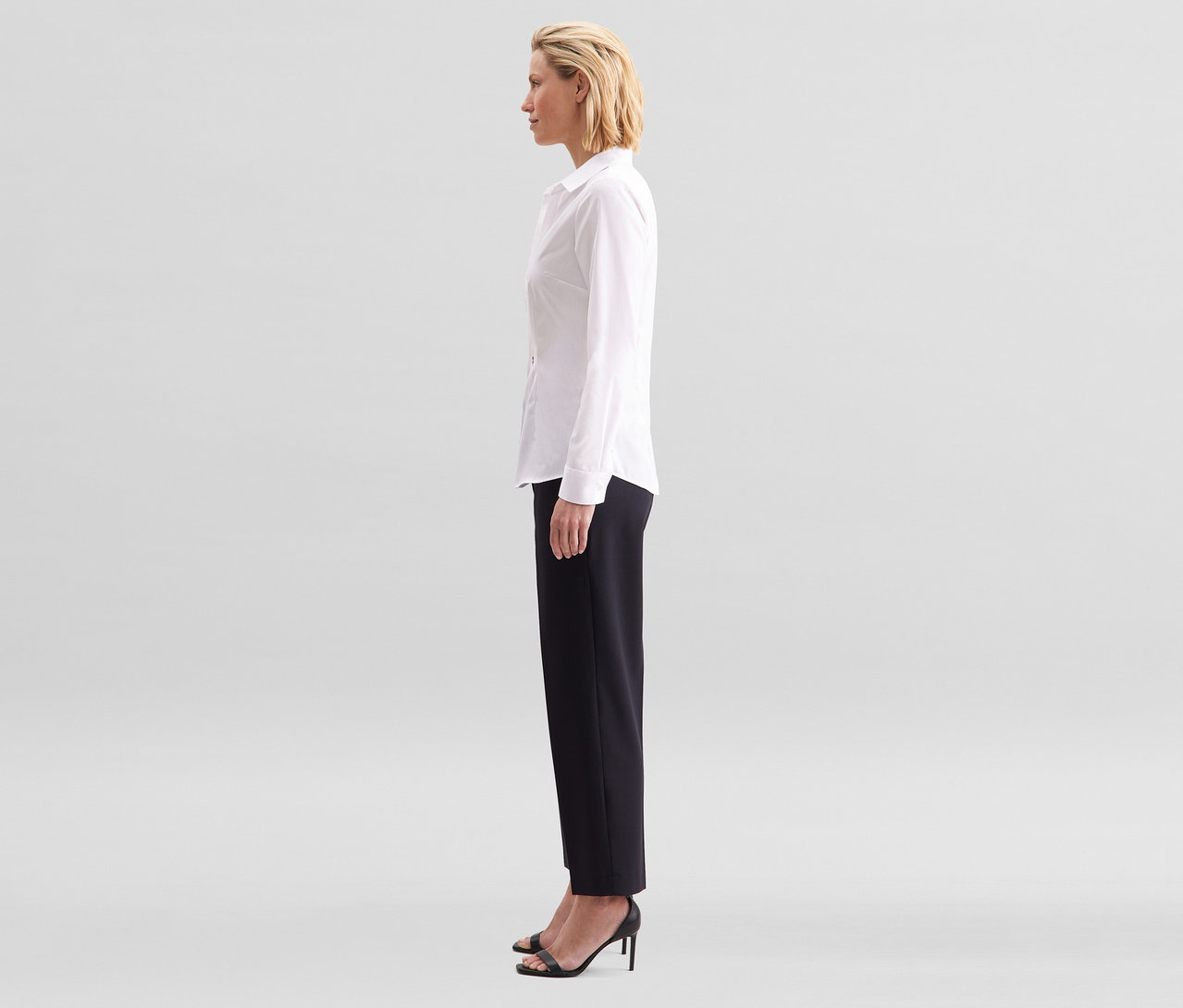 Žena z profilu, oblečená v bielej blúzke Seidensticker Slim Fit non iron a čiernych nohaviciach.