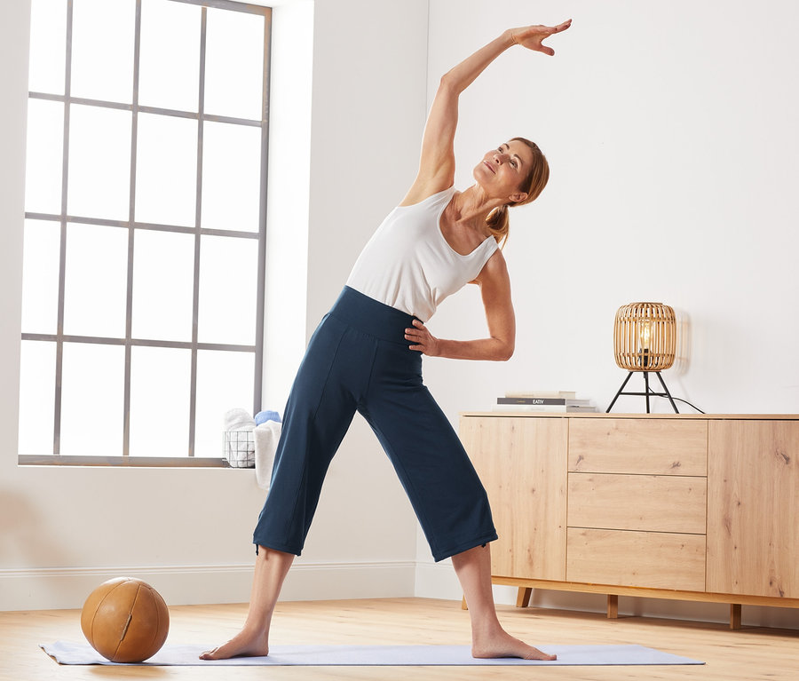 Žena sa na podložke na jogu naťahuje a má na sebe trojštvrťové športové nohavice.
