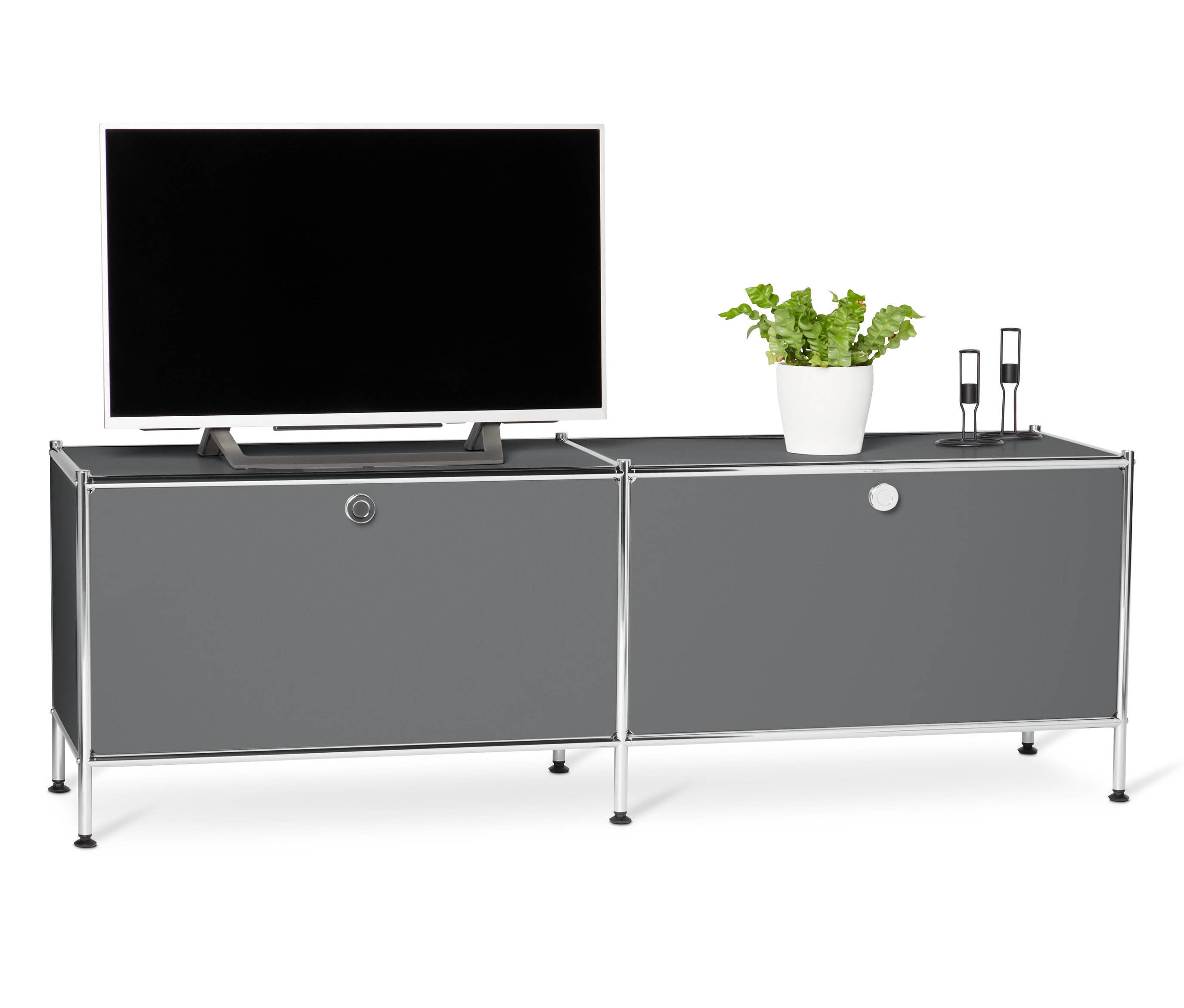 Televízor stojí na sivej kovovej nízkej skrinke »CN3« s výklopnými priehradkami.