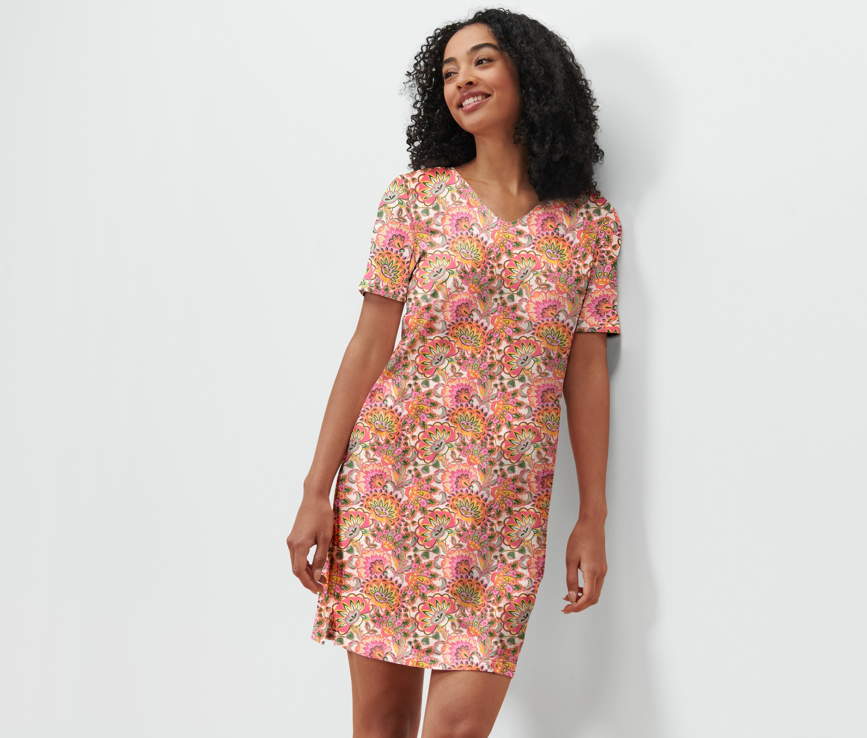 Žena v nočnej košeli s kvetinovým vzorom sa opiera o bielu stenu.