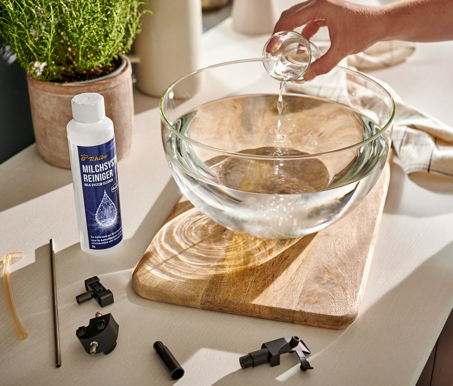 Ruka naleje číru tekutinu z odmerky do sklenenej misy s vodou. Vedľa misy stojí čistič mliečneho systému durgol® a súčiastky kávovaru.