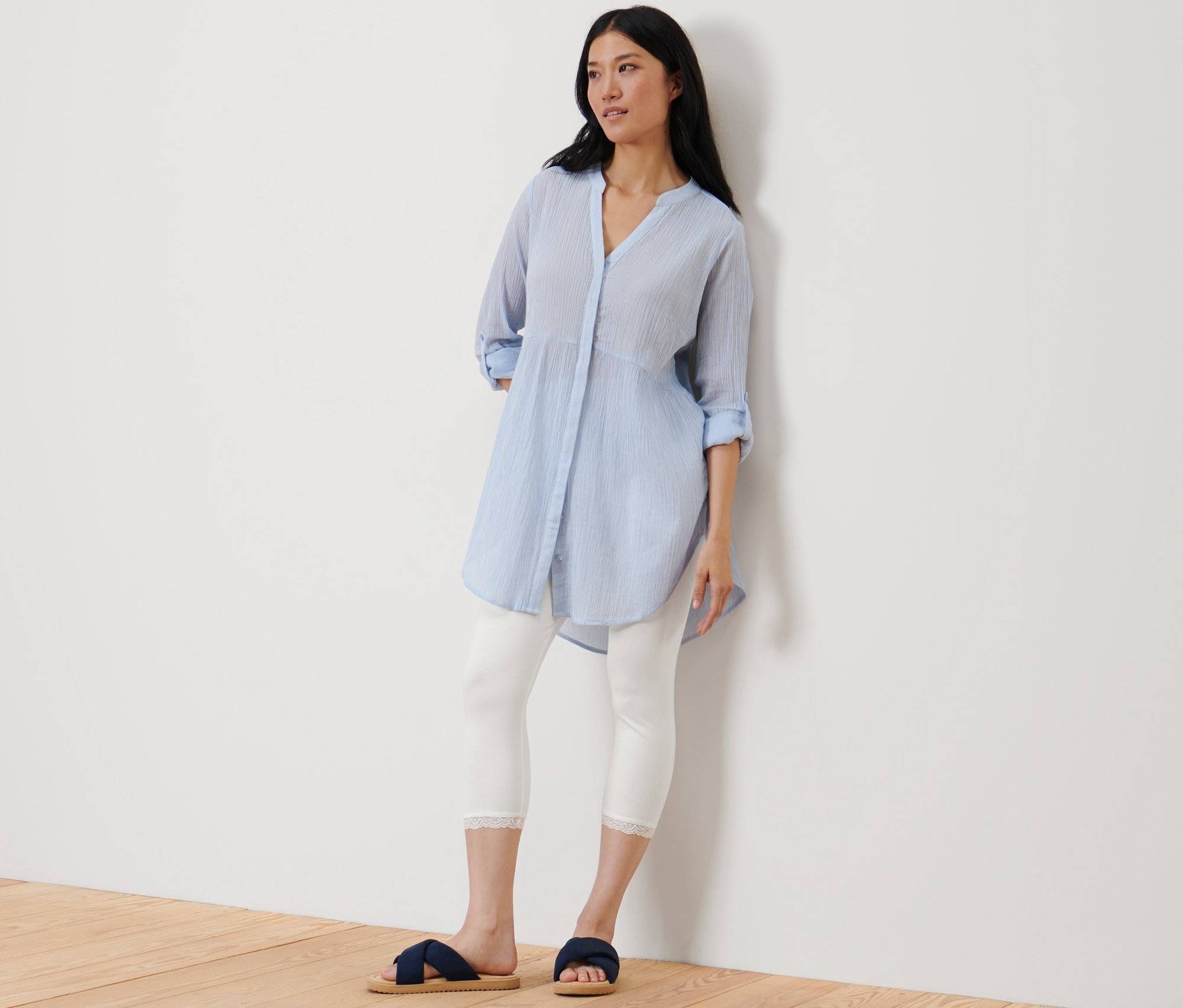 Žena stojí opretá o stenu a má na sebe biele trojštvrťové legíny s čipkovým lemom.