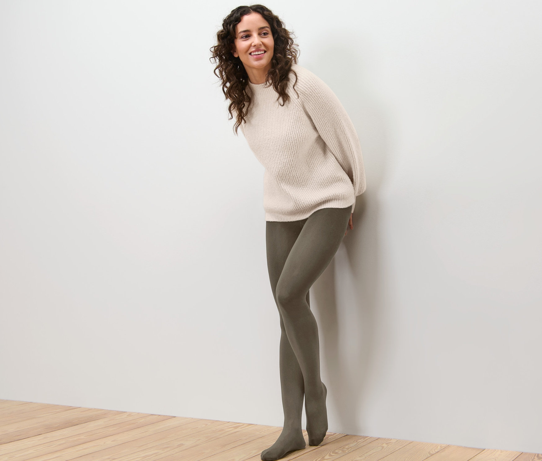 Žena opretá o stenu má na sebe termopančuchy a sveter.