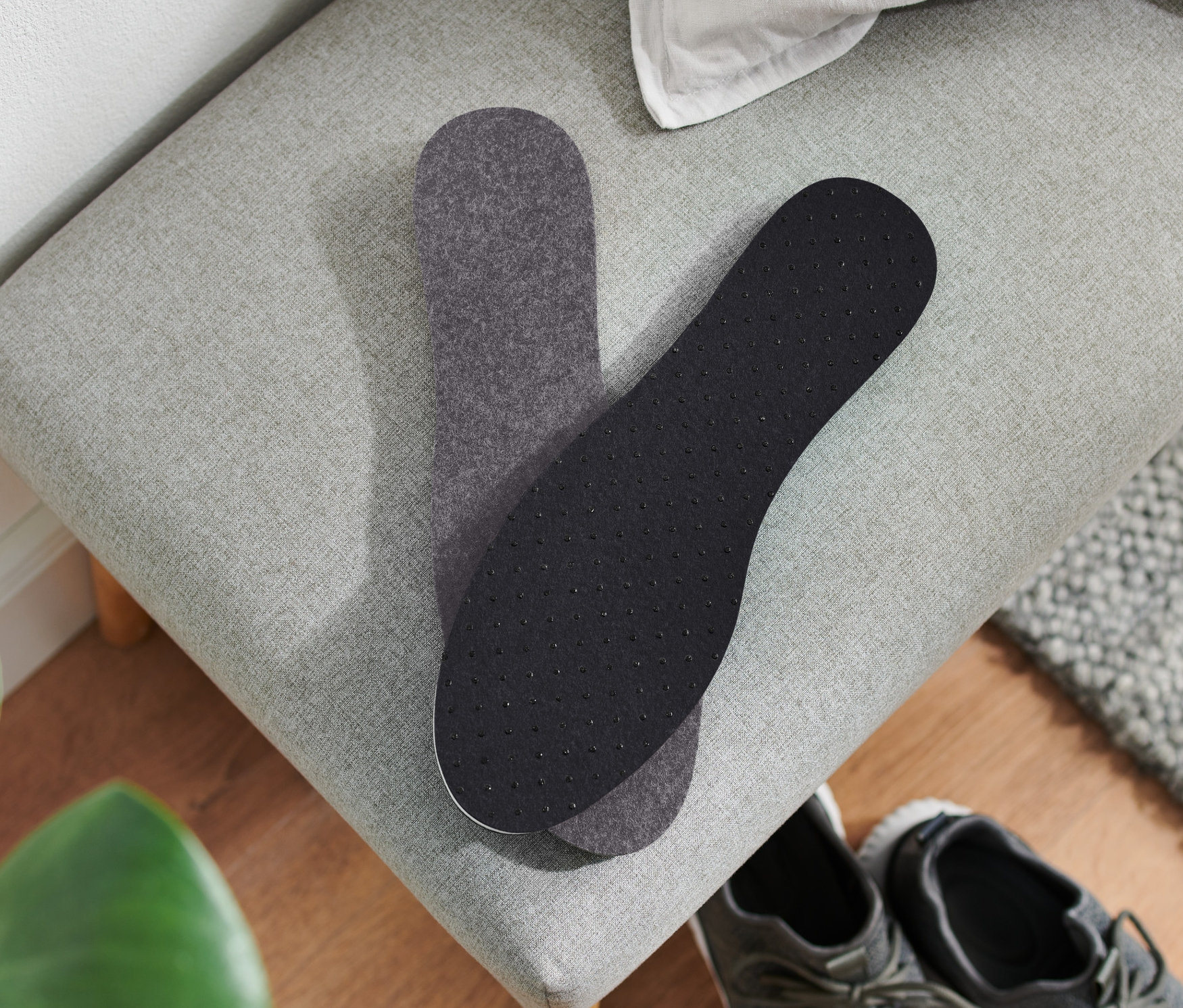 Dve termoizolačné vložky do topánok ležia na sivej lavici vedľa páru sivých topánok.
