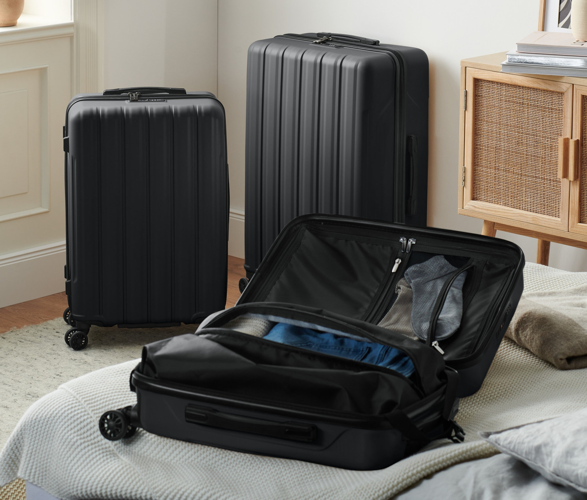 Tri čierne kufre s tvrdou škrupinou, jeden malý otvorený na posteli.