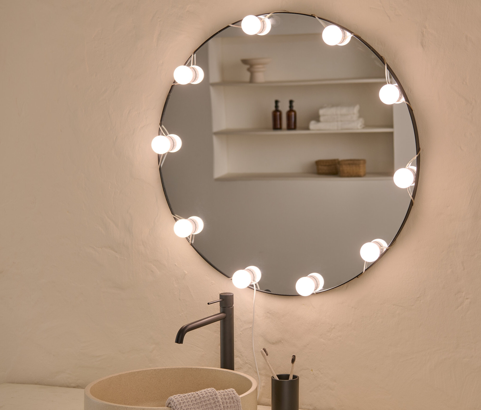 Kúpeľňa s umývadlom, batériou a okrúhlym zrkadlom s LED USB svetelnou reťazou.