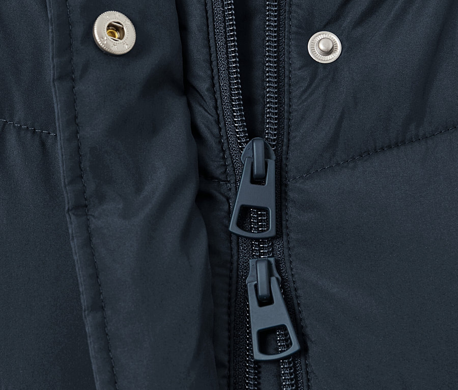 Detail tmavomodrého prešívaného kabáta s kapucňou zobrazuje zips a patentky.