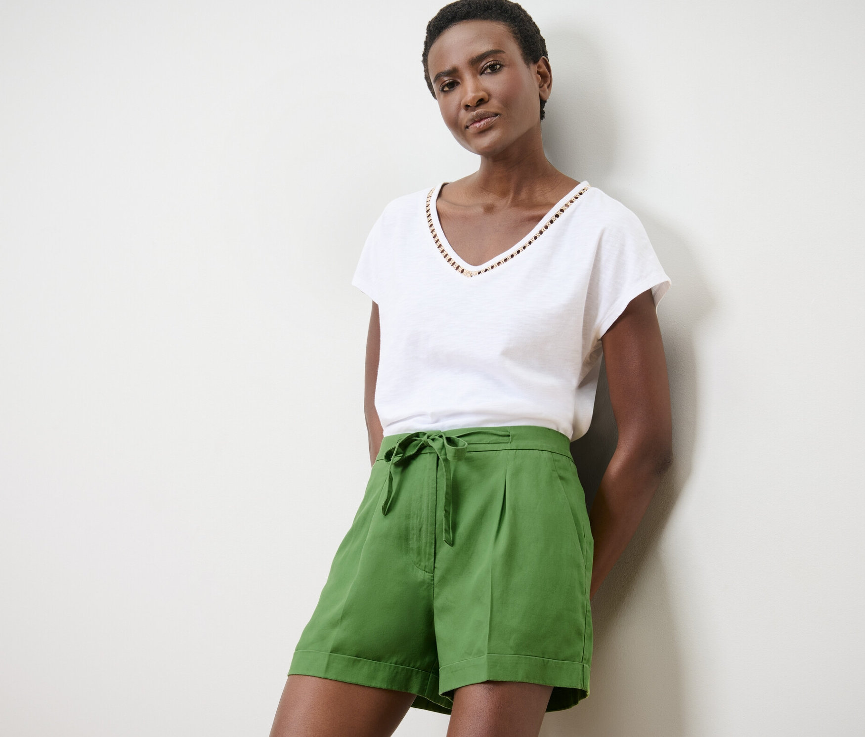 Žena pózuje v zelených ľanových šortkách a bielom tričku.