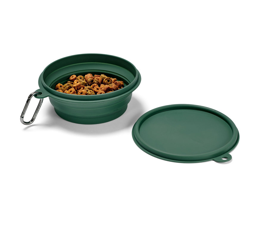 Zelená skladacia miska na žrádlo s karabínou, naplnená granulami, vedľa leží viečko.