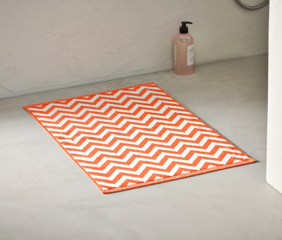 Oranžovo-biela predložka pred sprchovací kút leží na podlahe v kúpeľni.