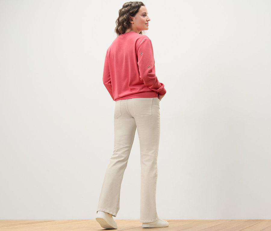 Žena stojí chrbtom k fotoaparátu a má na sebe krémovobiele bootcut džínsy – strih »Lou« a ružovú mikinu.