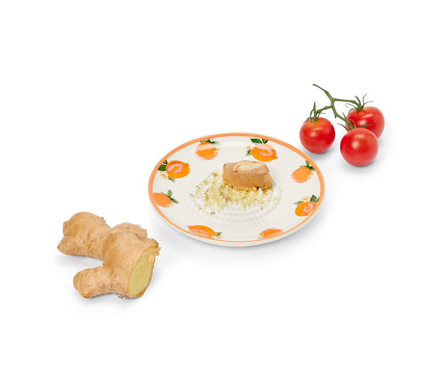 Kúsok zázvoru na tanierovom strúhadle, vedľa je celý zázvor a cherry paradajky.