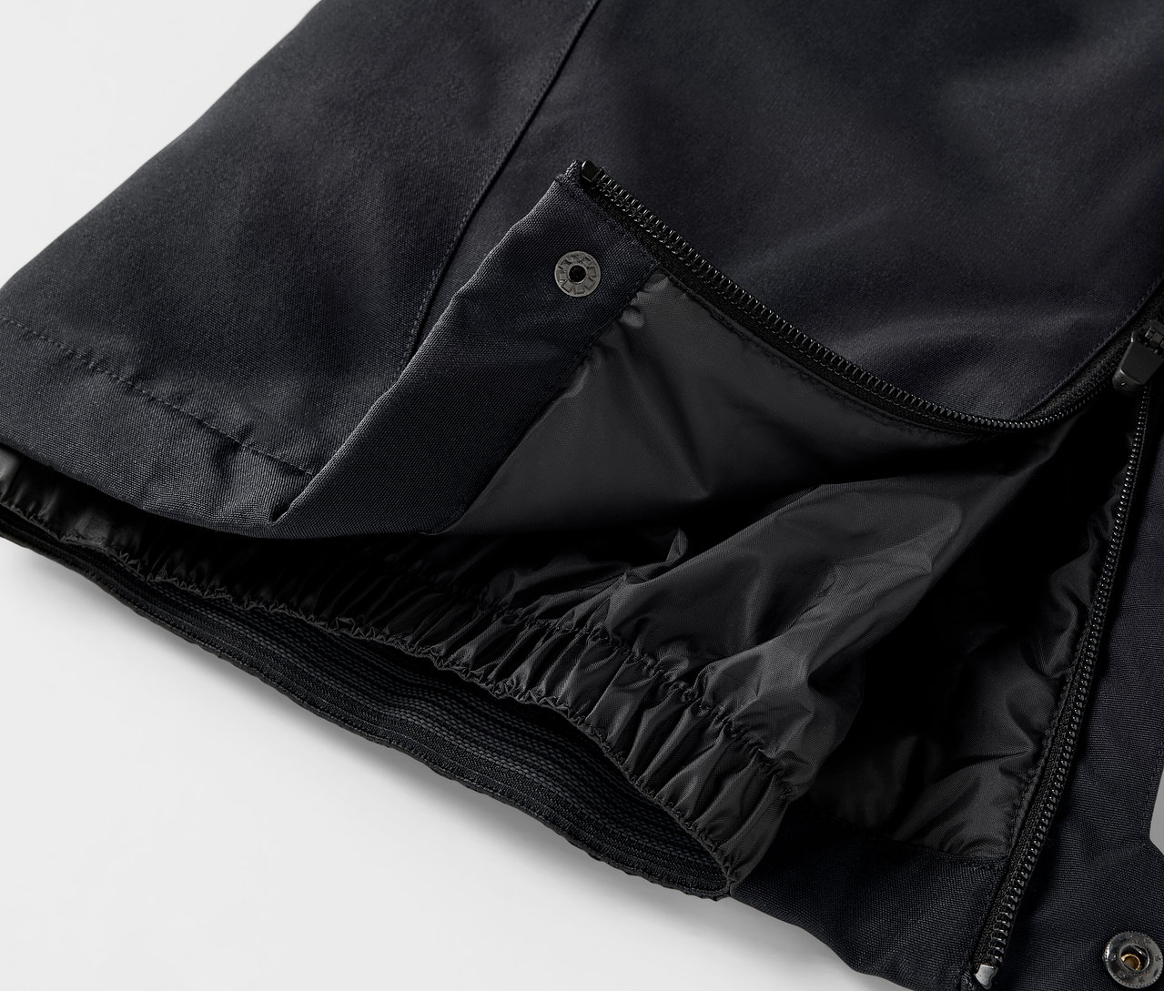 Detail čiernych nohavíc s rozopnutým zipsom a patentkou.