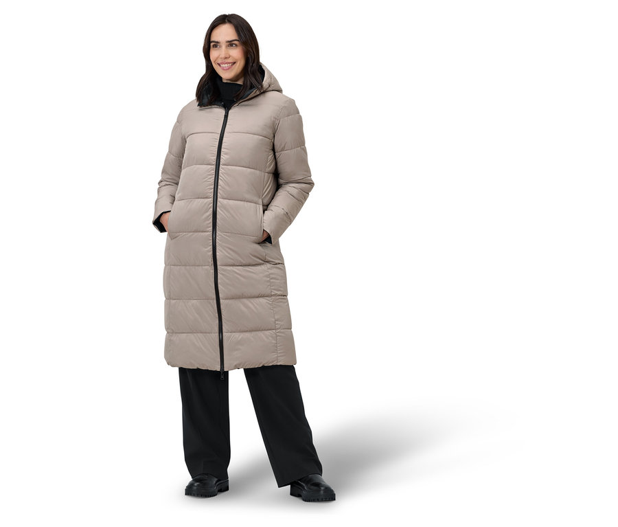 Žena pózuje v béžovom páperovom kabáte a čiernych nohaviciach.