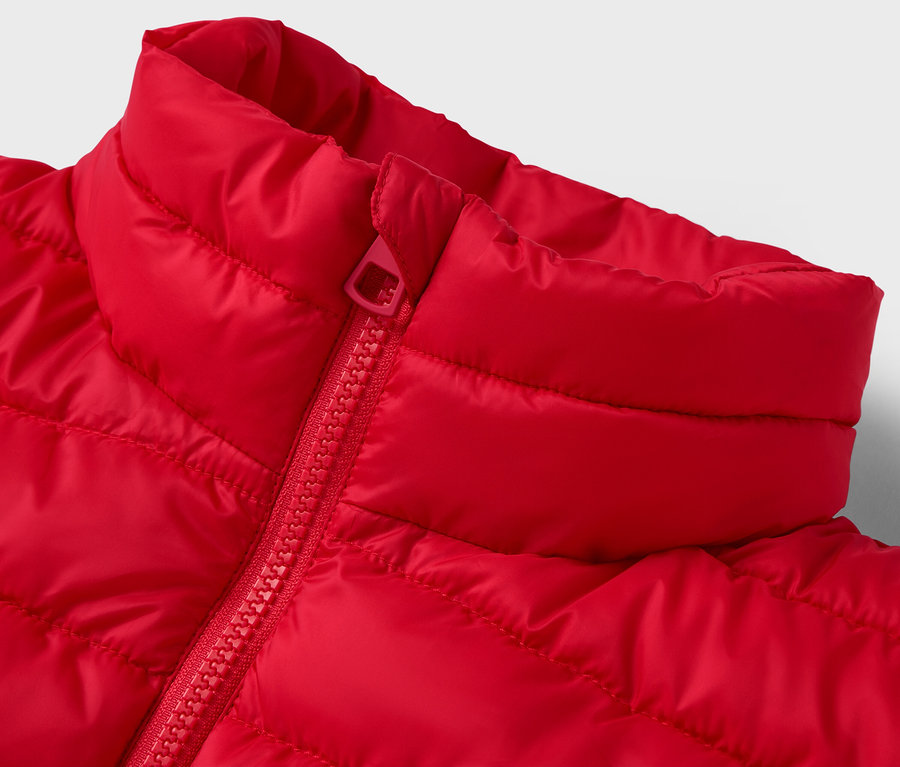 Detail červenej prešívanej bundy s golierom a zipsom.