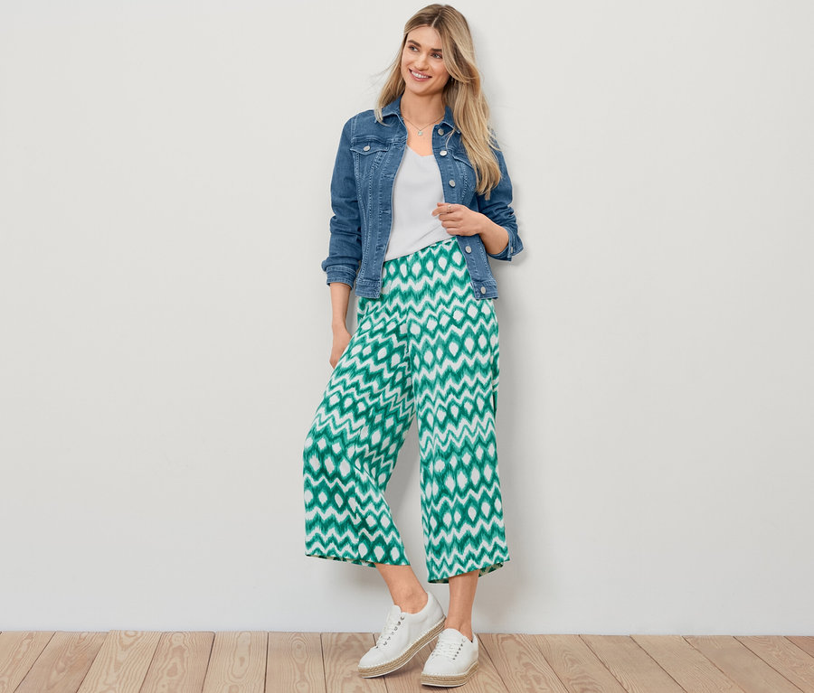 Blondínka pózuje v džínsovej bunde, bielom štruktúrovanom tričku a vzorovaných saténových nohaviciach.