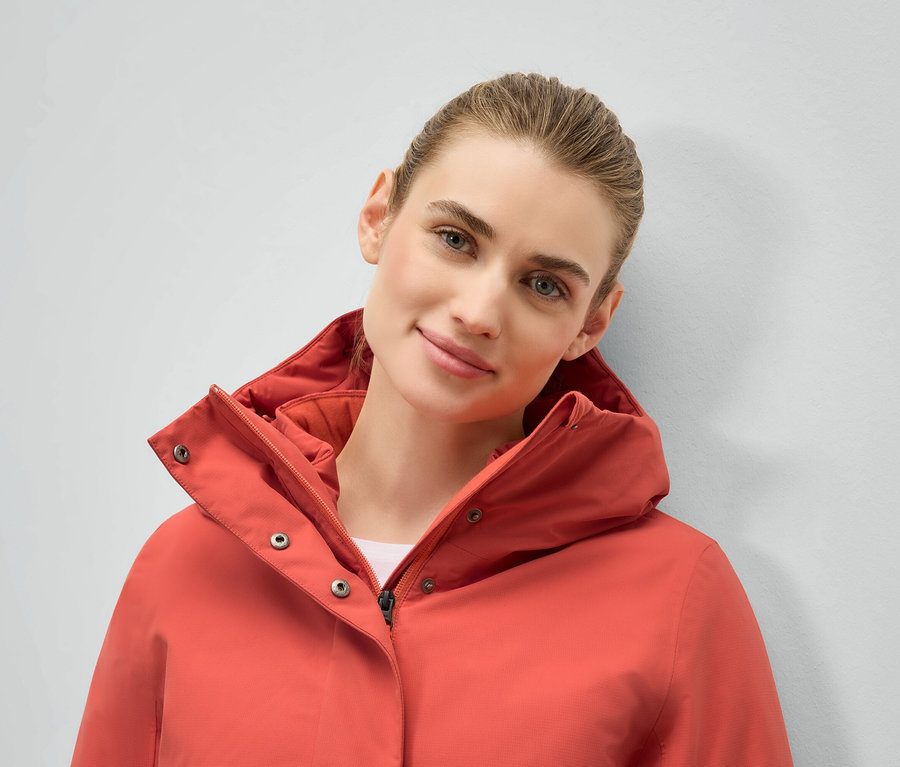 Portrét ženy v koralovej bunde s kapucňou.