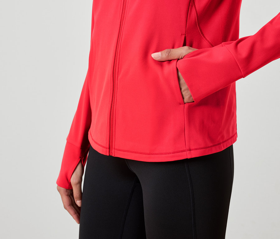 Žena má ruku vo vrecku červenej bundy a má na sebe čierne legíny.