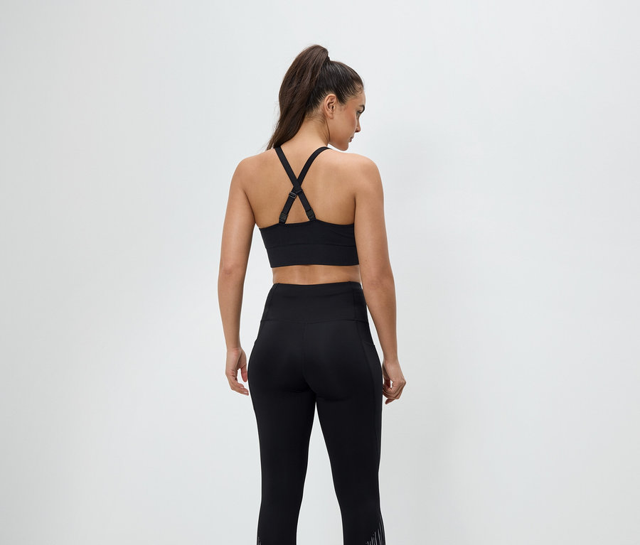 Zozadu je vidieť žena v čiernom športovom oblečení, má na sebe športovú podprsenku a legíny.