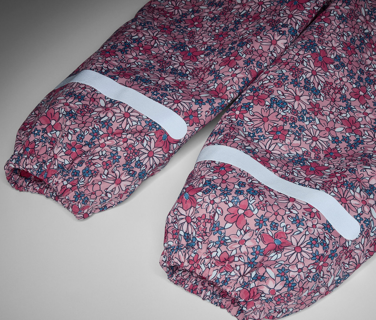 Detail detských termo nohavíc do dažďa s kvetinovým vzorom a reflexnými pruhmi.