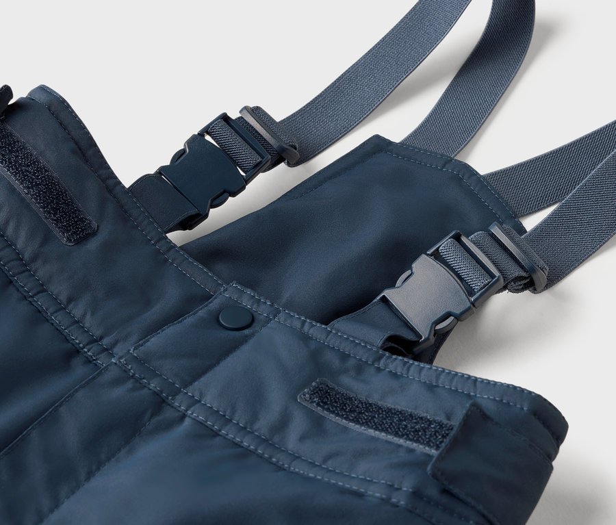 Detail modrých trakov s sivými popruhmi a plastovými sponami.