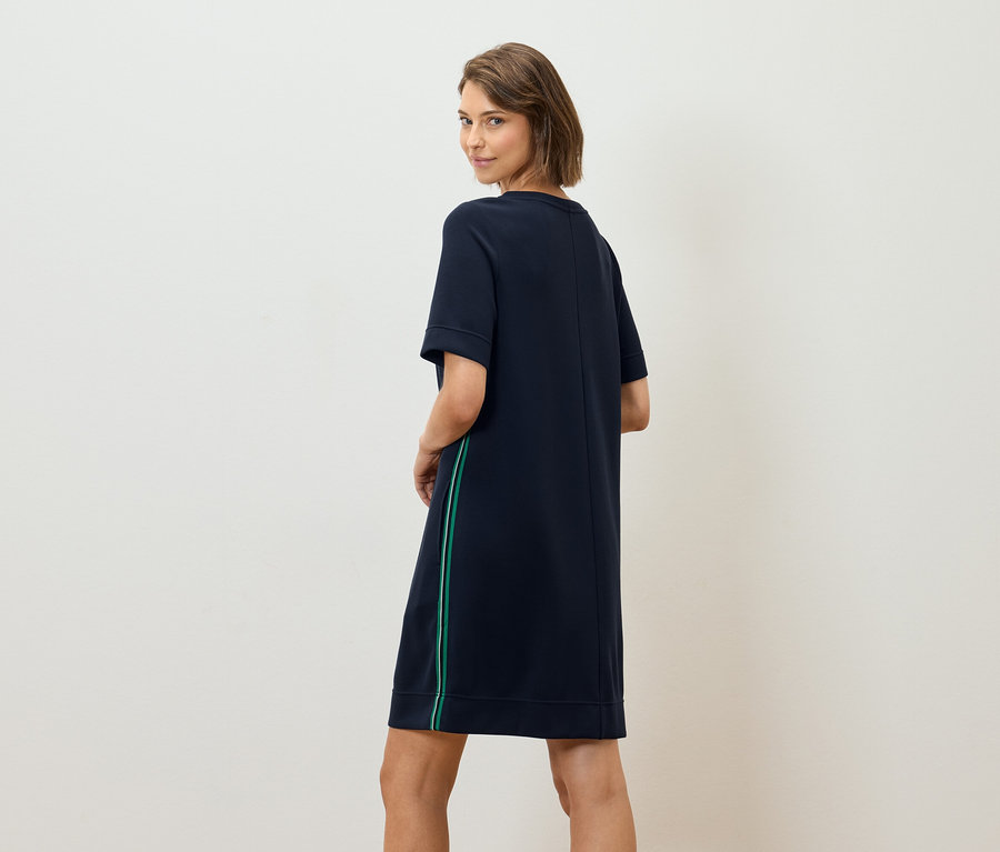 Žena sa pozerá cez rameno a má na sebe tmavomodré tričkové šaty so zeleným prúžkom.