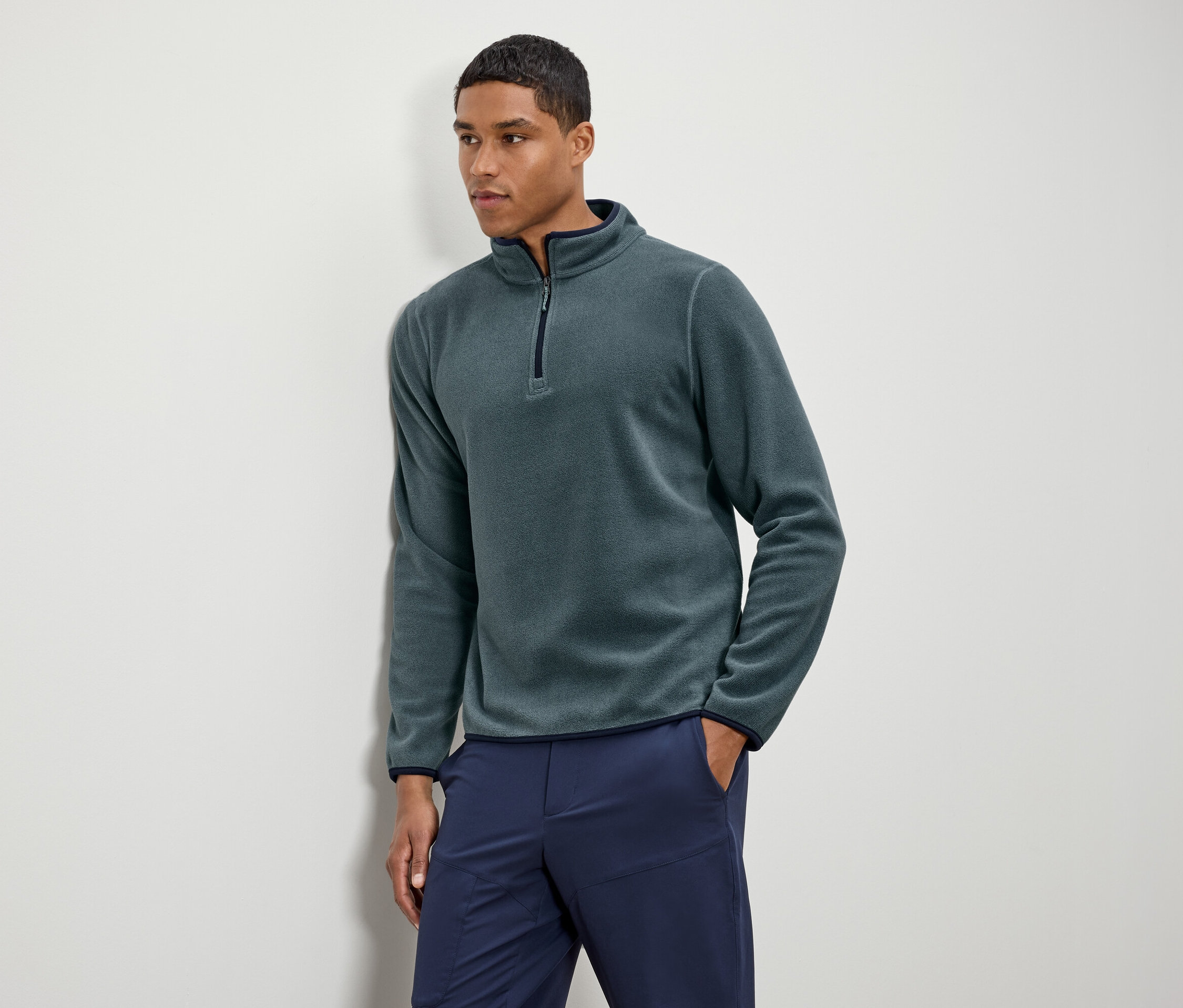 Muž má na sebe zelenú flísovú mikinu s tmavomodrými nohavicami.