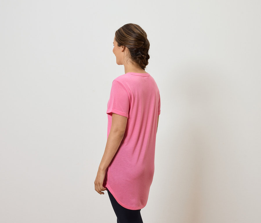 Žena chrbtom k fotoaparátu má na sebe ružové tričko a tmavé nohavice.