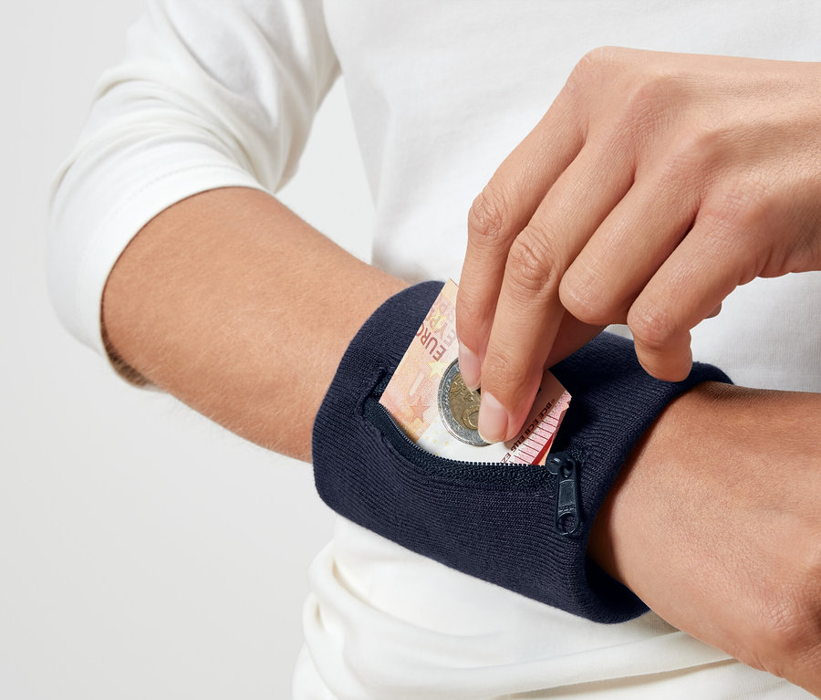 Osoba vkladá eurovú mincu do námorníckej modrej náramkovej peňaženky.