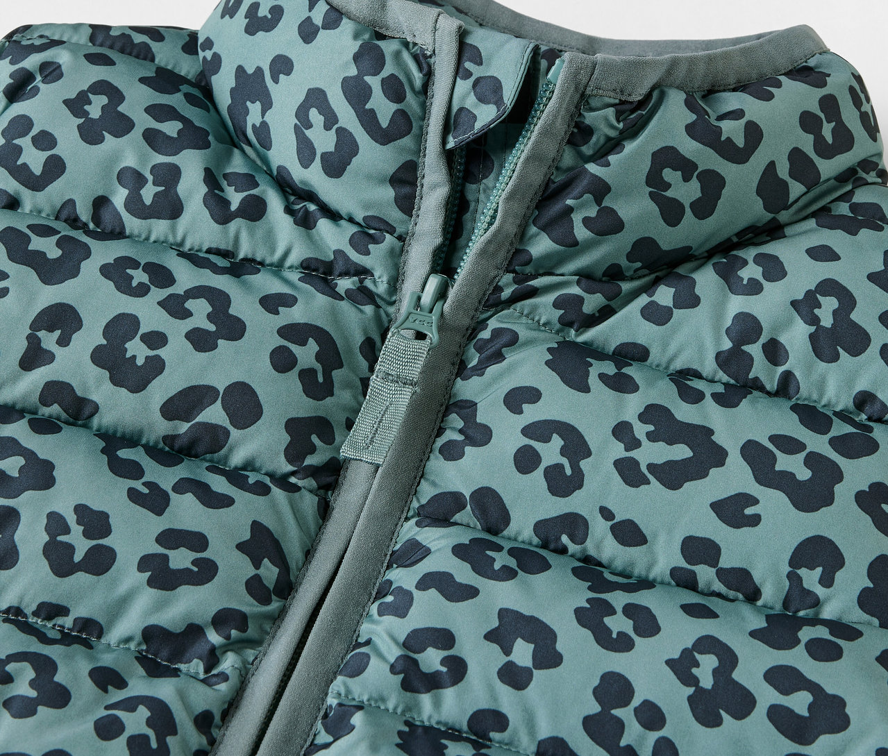 Detail detskej prešívanej vesty so zvieracou potlačou a zipsom.