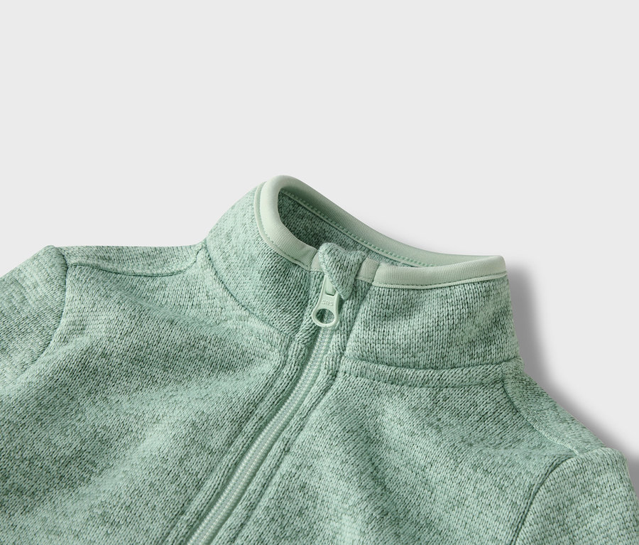 Detailný záber na svetlozelenú flísovú bundu na zips.