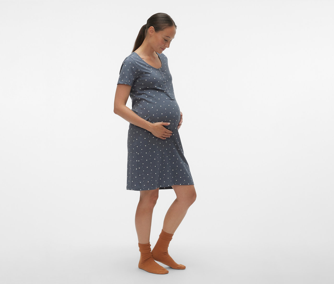 Tehotná žena v profile má na sebe modrú nočnú košeľu MAMALICIOUS »MLMIRA« s bielymi bodkami a hnedé ponožky.