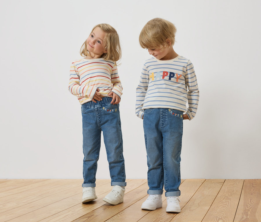 Blondínka a blond chlapec stoja vedľa seba a majú na sebe pruhované tričká s dlhým rukávom a džínsy.