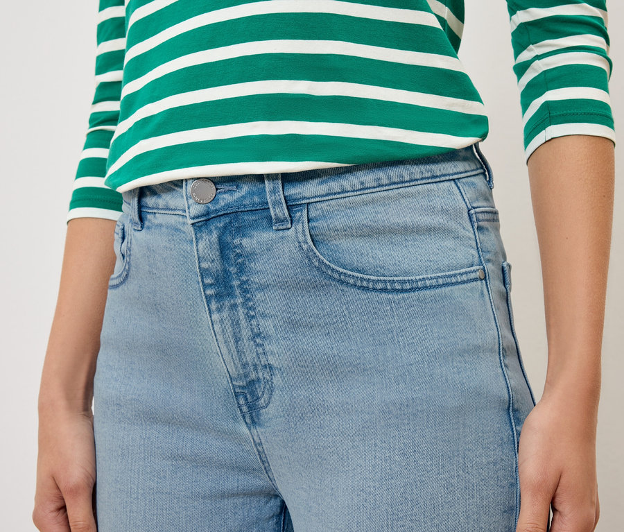 Detail osoby v svetlomodrých džínsoch a zeleno-bielo pruhovanom tope.