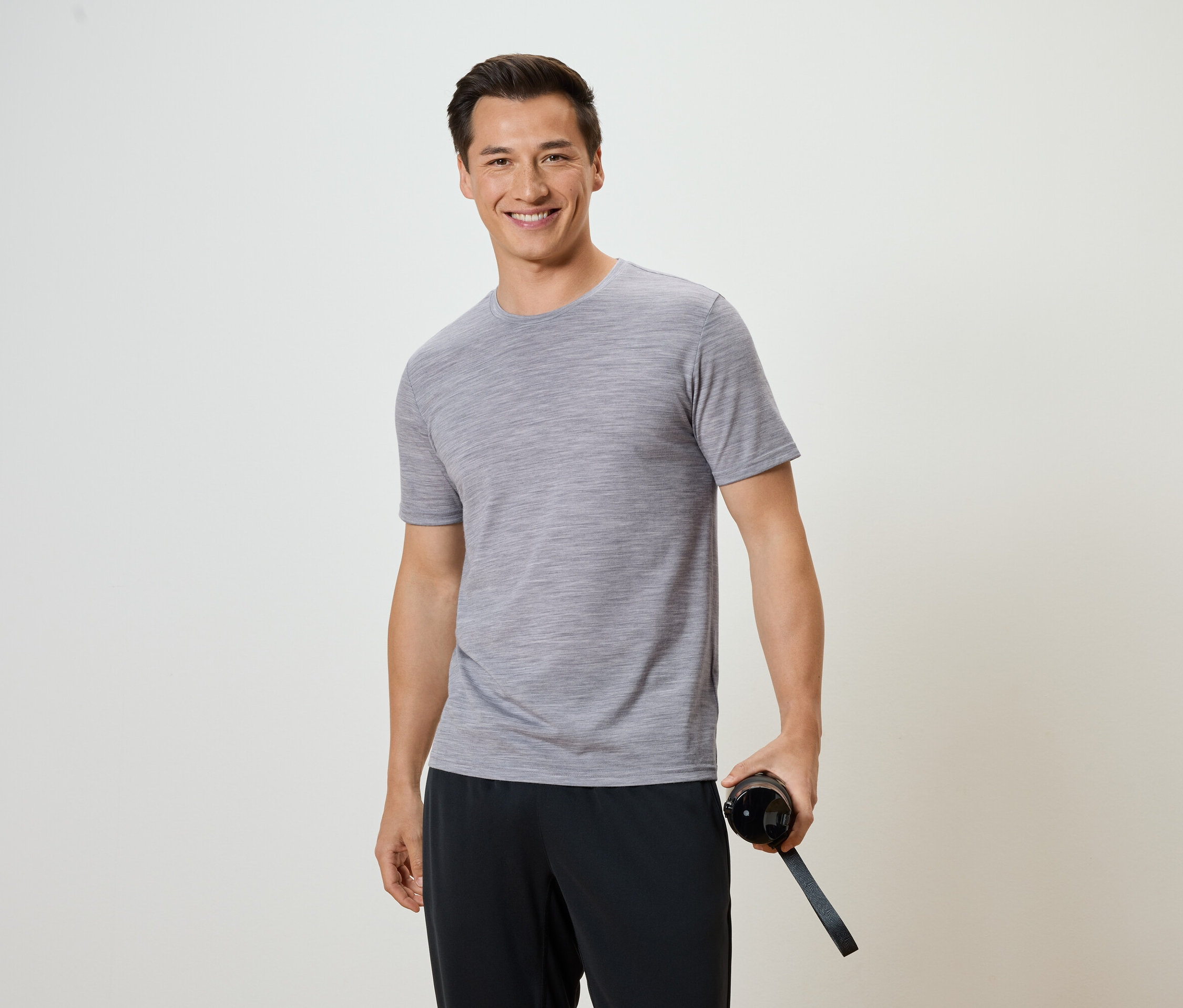 Muž v sivom tričku a čiernych nohaviciach drží fľašu s vodou.